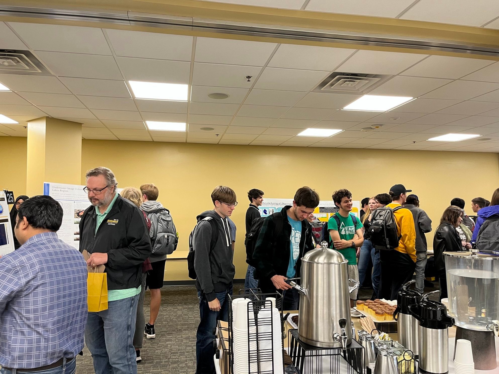Students and faculty attend the Student Poster Competition Attendees looking at posters and getting food from a buffet.