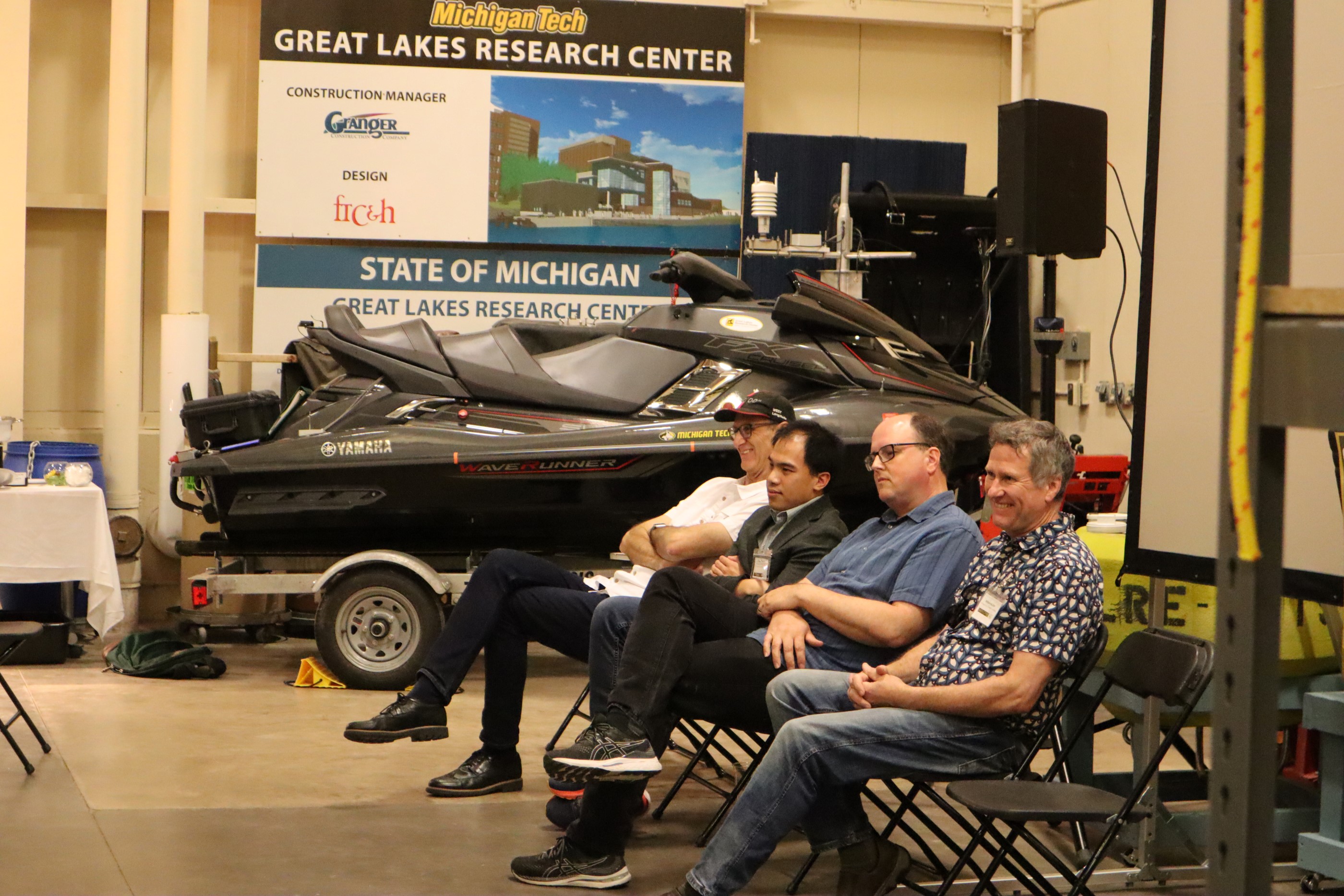 The AI in Academia and Industry Panel, featuring (from left) Jon Garibaldi, Vinh Nguyen, Shane Mueller, and William Buller. Panel members sitting in chairs in front of a wave runner.