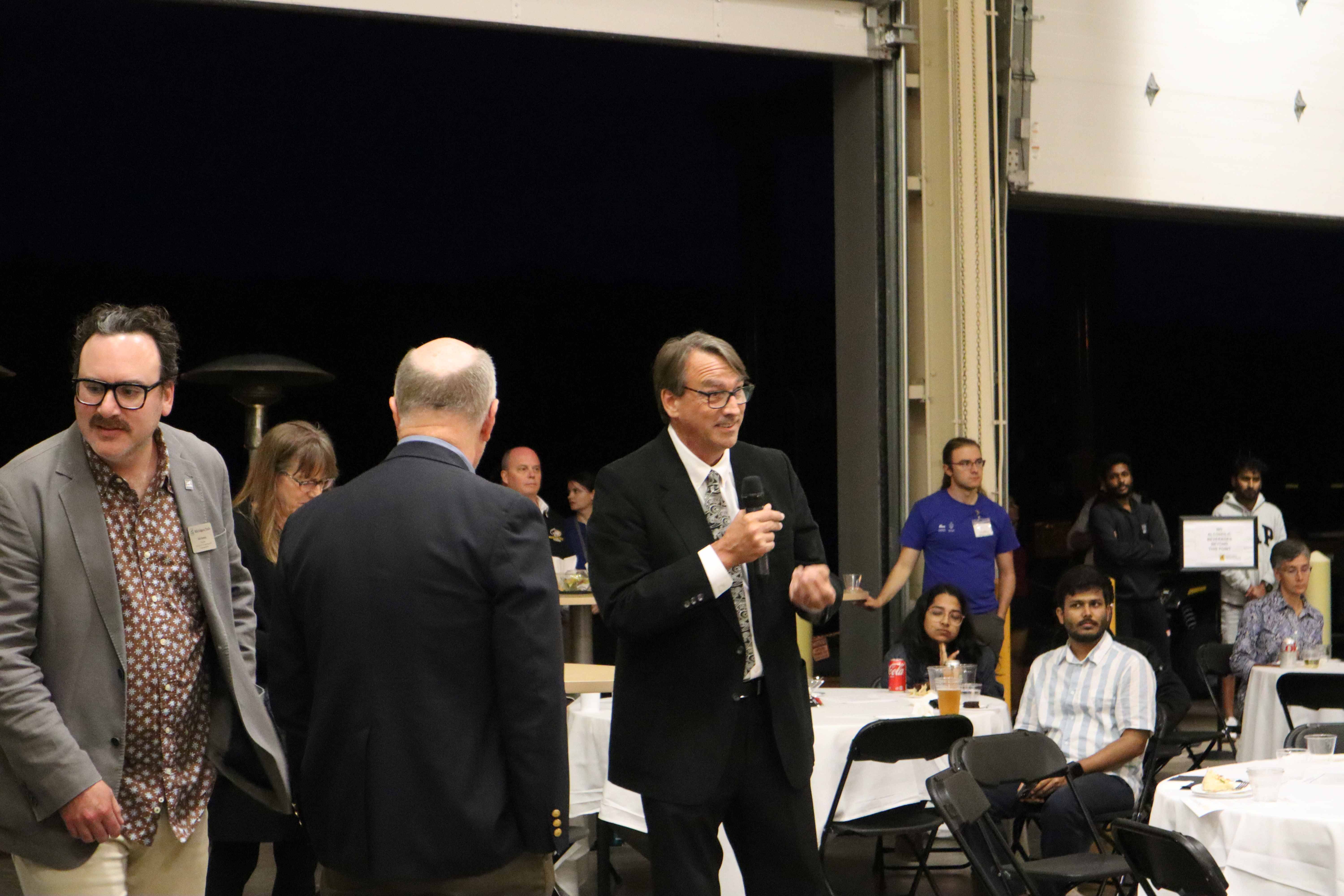 Randy Berry speaking during the Banquet. Randy Berry speaking and other attendees standing and sitting.