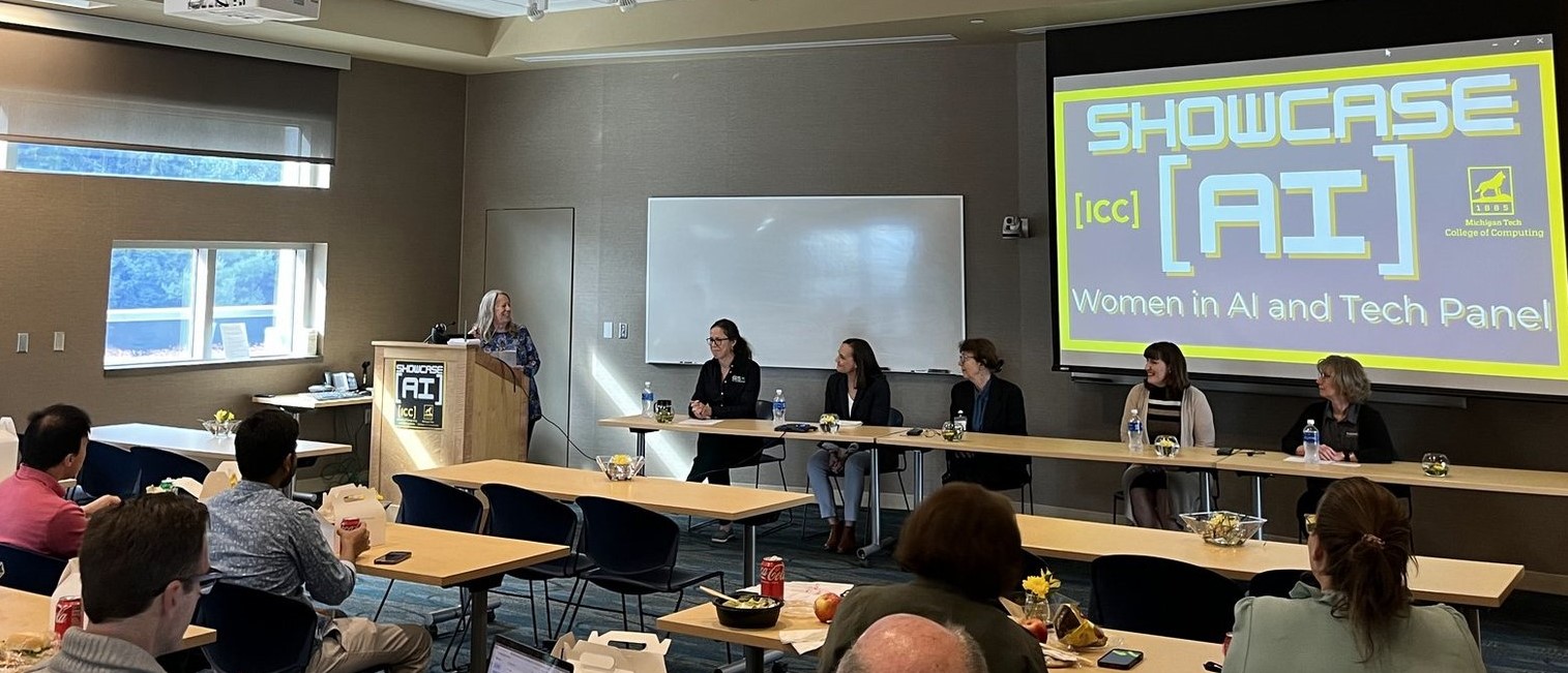 The Women in IT and Tech Panel
 Five women sitting at a table in the front of the room with another at a podium.