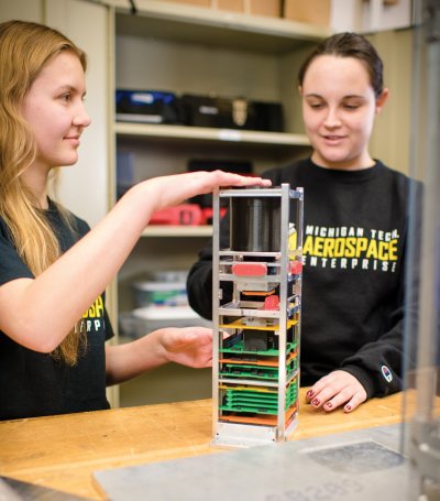 Two students working on a small satellite.