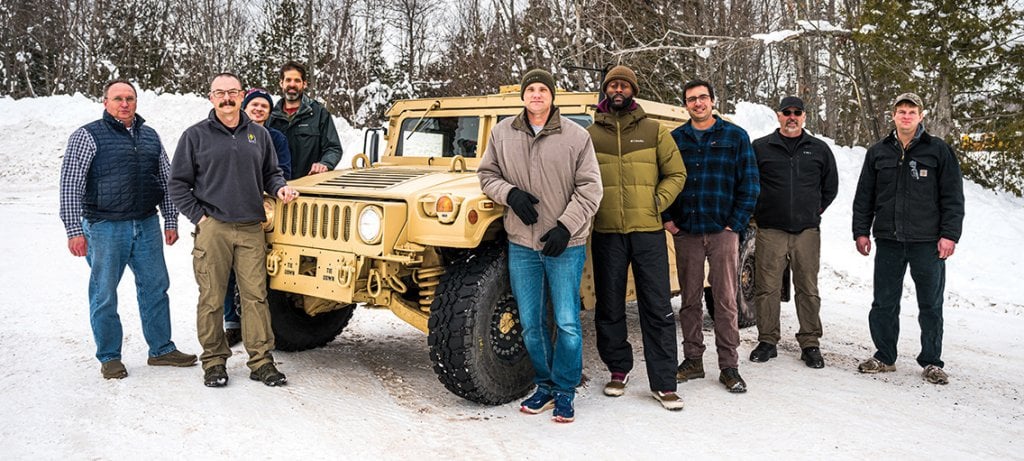 Nine people standing around the vehicle for a group photo.