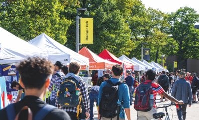 Students walking through campus with several vendor tents set up.