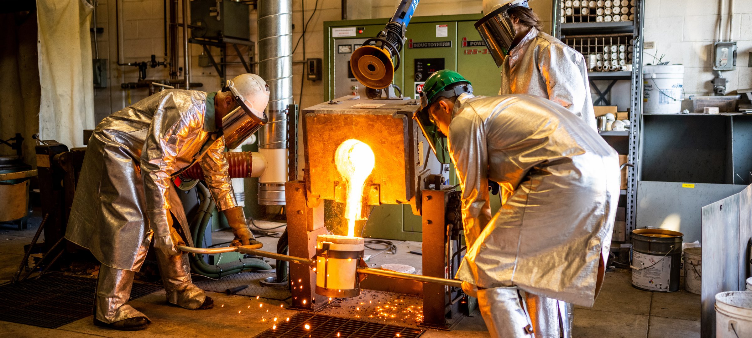 Melted metal being poured into a holder held by two researchers with one operating the machine.