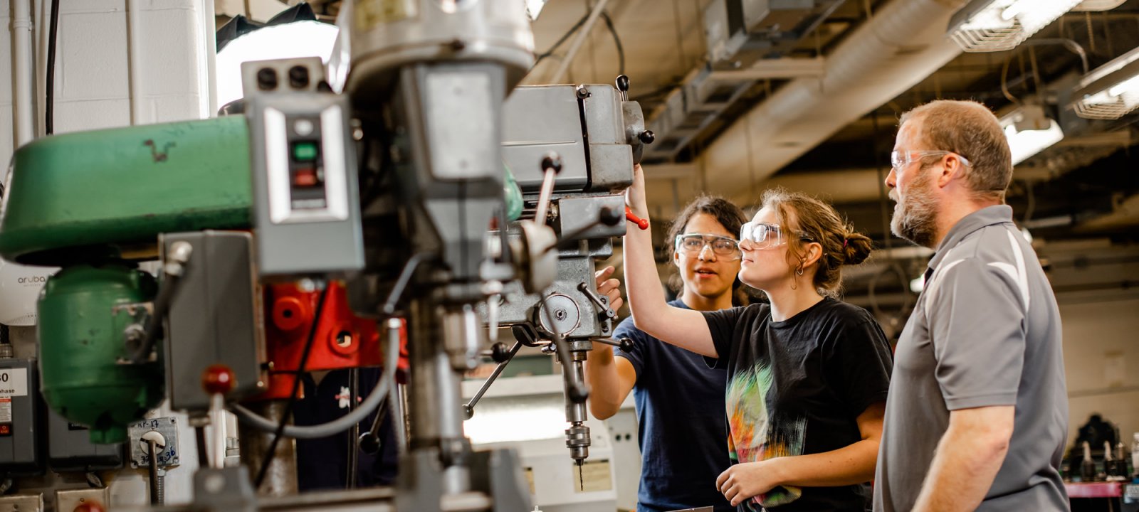 Professor supervising two students using equipment in the shop.