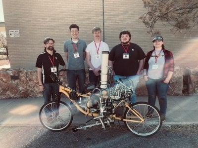 Five team members standing outside near a bicycle.