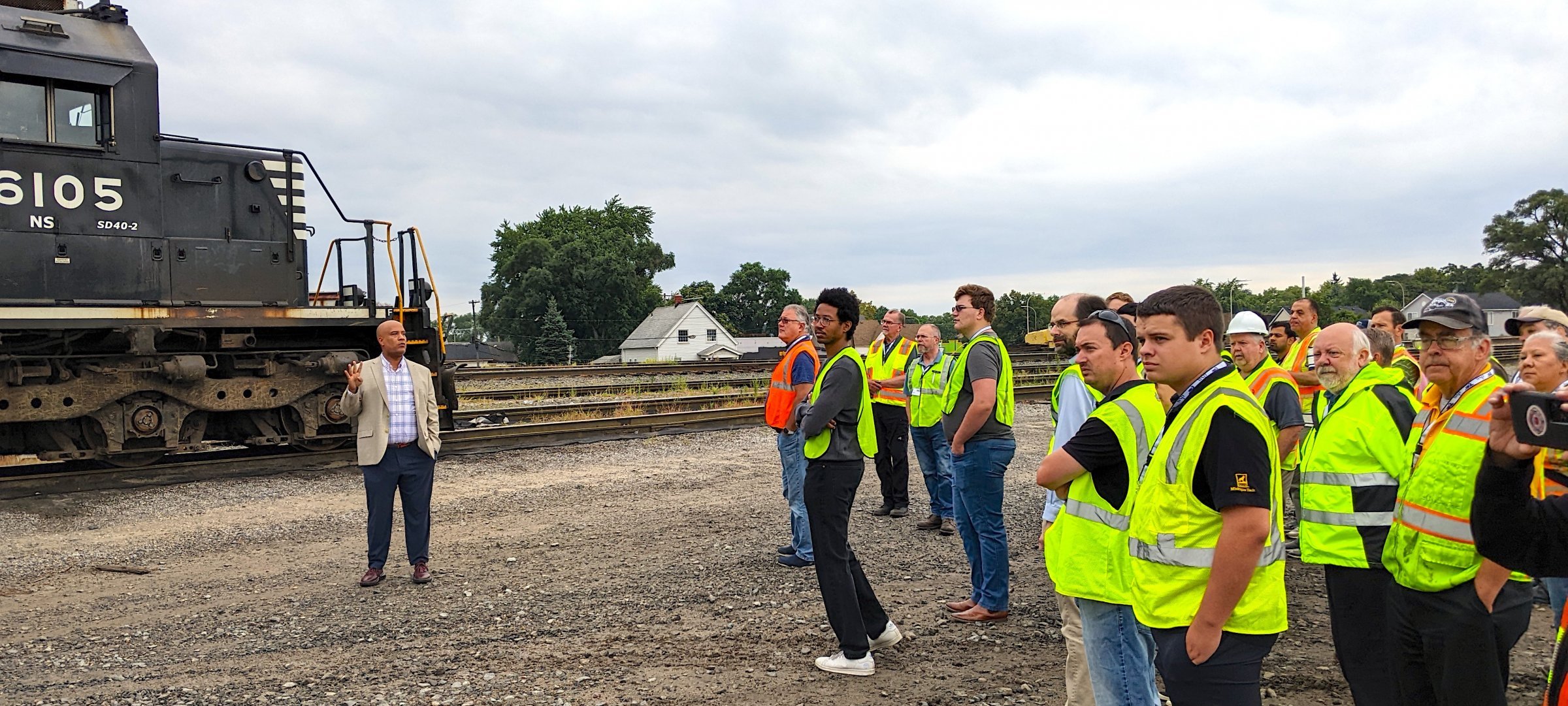 Speaker talking to rail conference participants outside next to a train engine