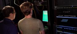 Professor and student looking at green computer screen in server room.