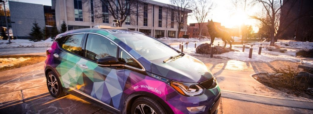 Safety is the driving force behind people's concerns with autonomous vehicles. Ironically, they could make driving a much safer activity—but the novelty of the technology changes people's perceptions. A car with a bright wrap of aurora borealis colors is backlit by the setting sun on Michigan Tech's campus
