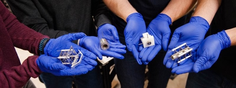 Gloved hands hold small nanosatellites.