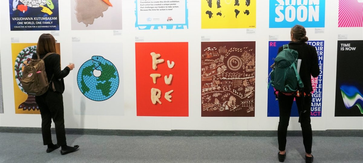 Students observe an art installation in one of the halls at COP25. Image Credit: Jessica Daignault Two people look at posters on a wall.