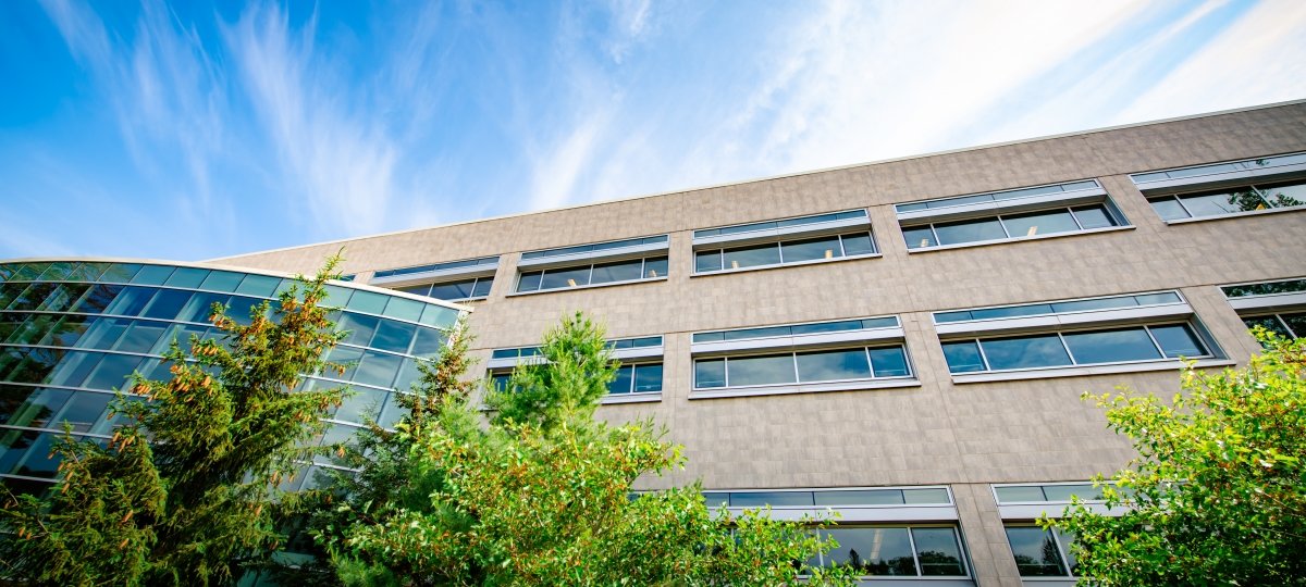 The 3D printers have been humming inside Van Pelt and Opie Library since spring 2020, part of the process of manufacturing PPE for the campus and community. Exterior shot of a stone library building with evergreens and deciduous bushes in front with a bank of all windows to the left and blue sky above outside in summer.