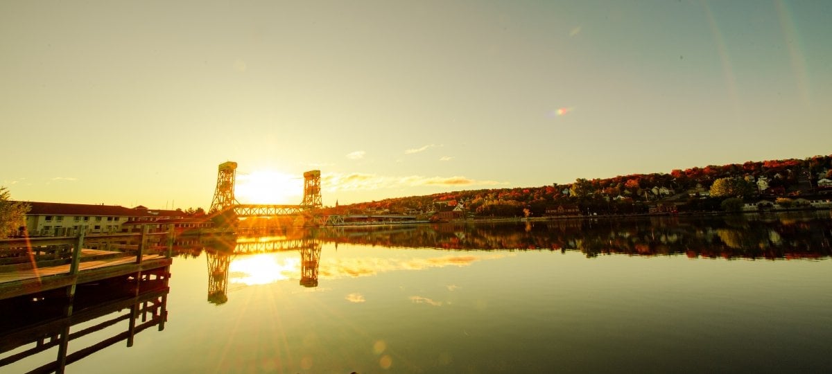 How people develop COVID-19 symptoms isn’t a flat line, but a bell curve, which has changed the CDC quarantine period recommendations. The sun sets behind the Portage Lake Lift Bridge.