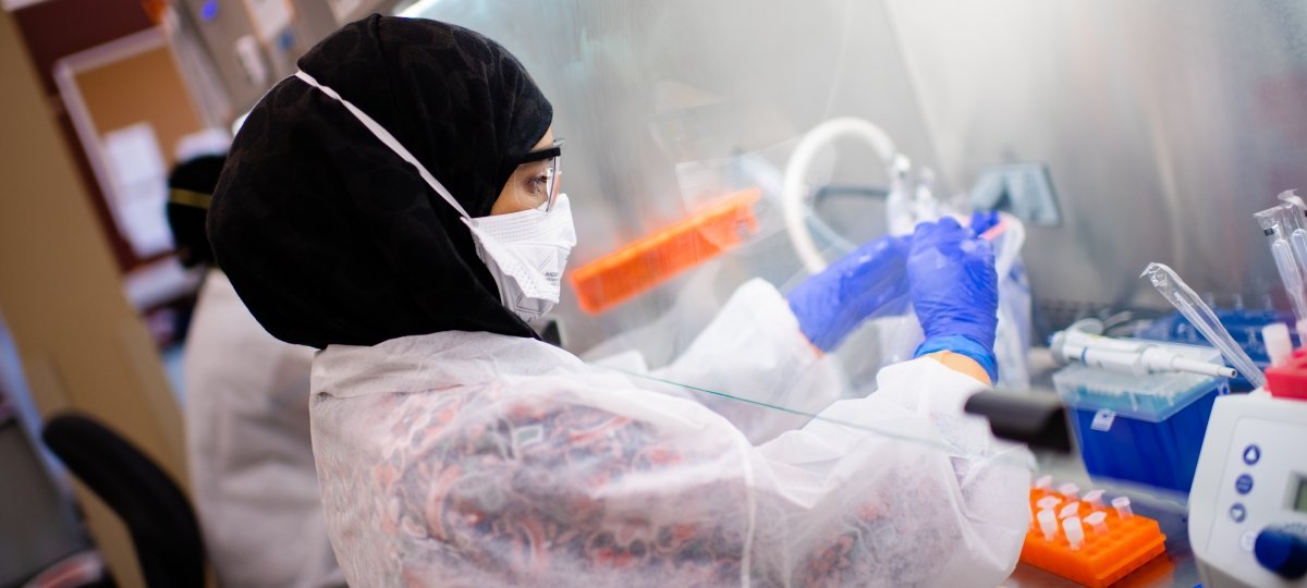 A staff members extracts SARS-COV-2 genetic material. Caryn Heldt helps run the COVID-19 testing lab at Michigan Tech and has studied vaccine manufacturing for 15 years. person in disposable PPE working in a lab with their hands under a hood