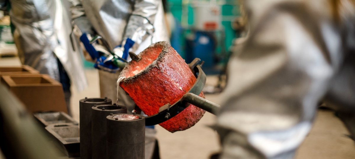 Students from the Department of Materials Science and Engineering work in the Michigan Tech foundry. Two people in fire-resistant clothing pour melted metal from a red-hot crucible.