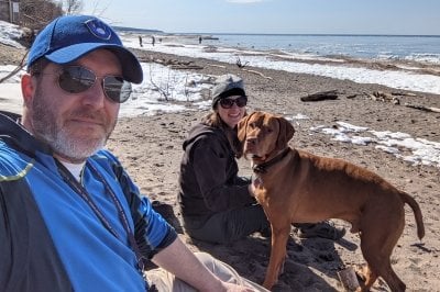 Andrew Barnard, wife Becky Barnard, and their dog (a brown Vizsla) recline on a snowy Lake Superior beach.