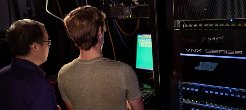 Professor and student looking at green computer screen in server room. 