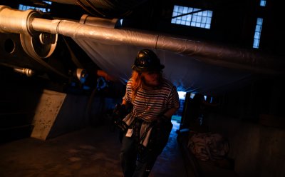 Student wearing a hard hat, ducking under a pipe while walking through the dark mine hoist.