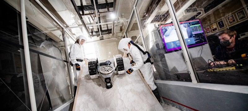 Researchers wearing personal protective equipment test a rover in the Planetary Surface Technology Development Lab's regolith sandbox.