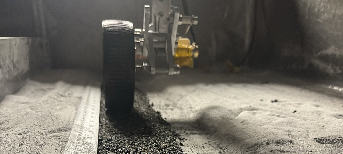Using simulated lunar dust and robotic technologies, Michigan Tech and SpaceFactory collaborated to create lunar asphalt, an innovative new material that affects the future of planetary surface transportation. (Image credits: All photos courtesy SPACEFACTORY and PSTDL) Straight-on view of a lunar rover wheel going over asphalt in the middle of sand.