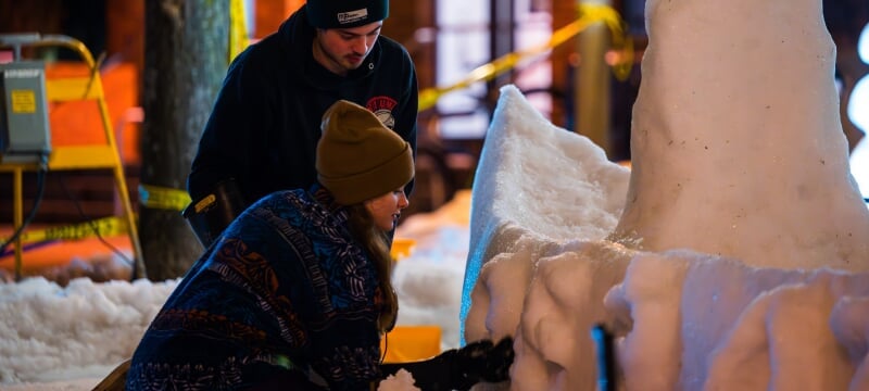 Two students working on adding details to a snow statue during all-nighter.