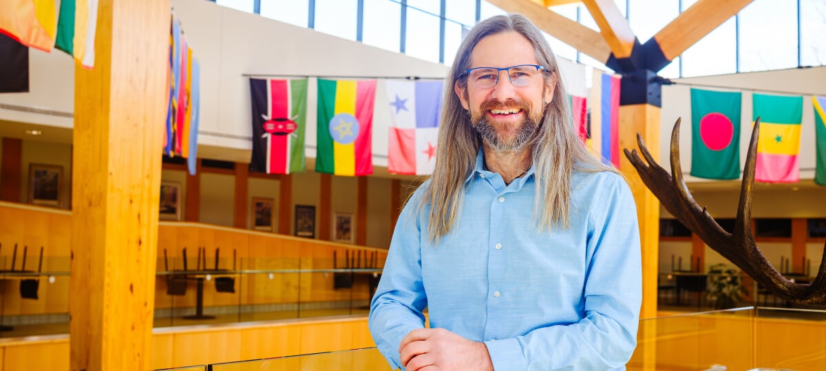 Michigan Tech researcher and renowned wildlife ecologist John Vucetich, shown here in the atrium of the College of Forest Resources and Environmental Science, has been honored with the University’s 2025 Research Award. John Vucetich in the CFRES atrium with international flags hanging behind him.