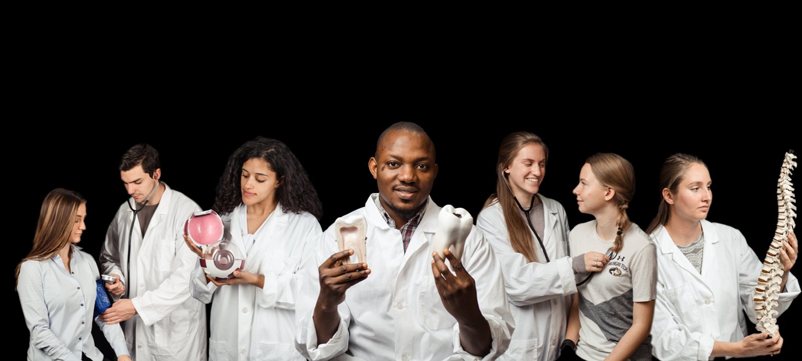 Pre-Health Professions students in lab coats holding different objects with some interacting with student patients