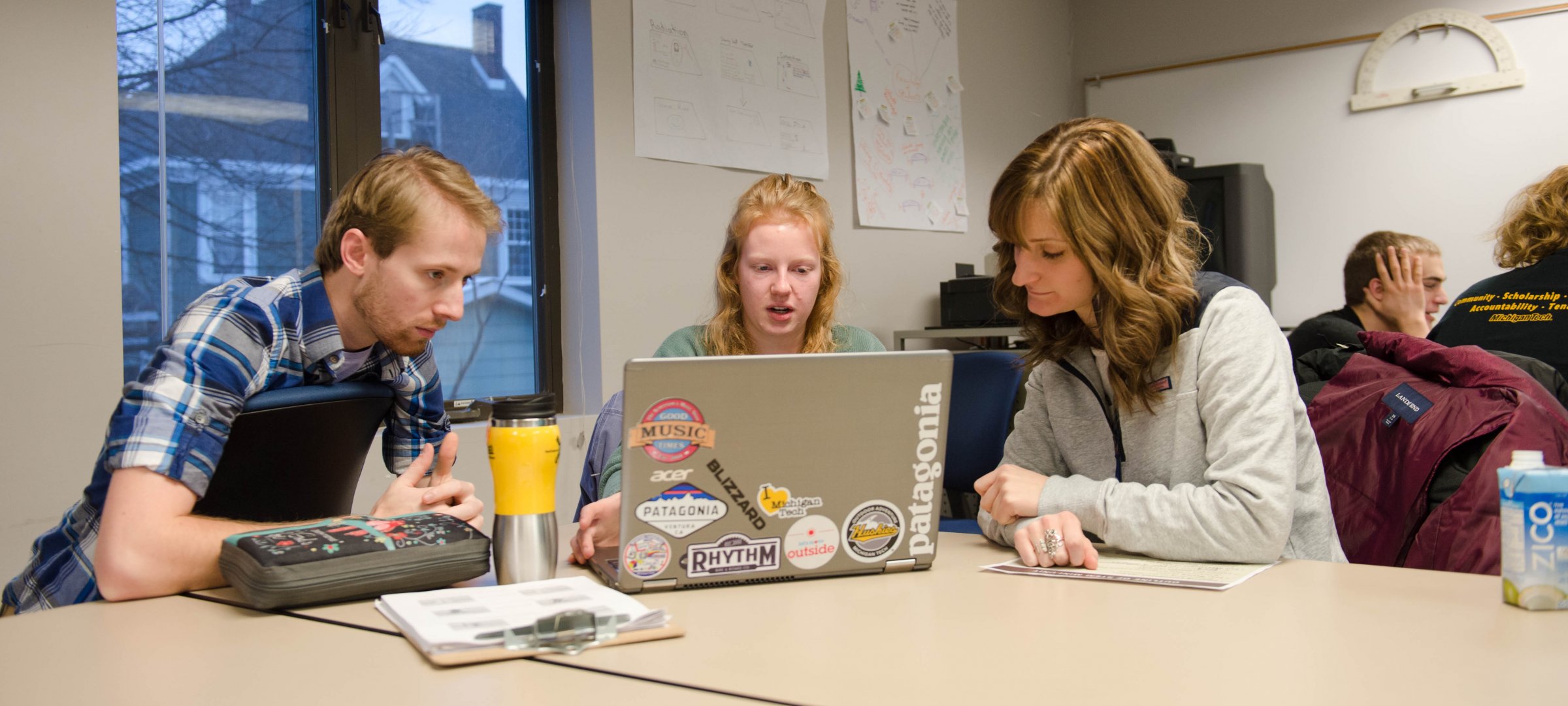 Three students interacting with a laptop in a classroom