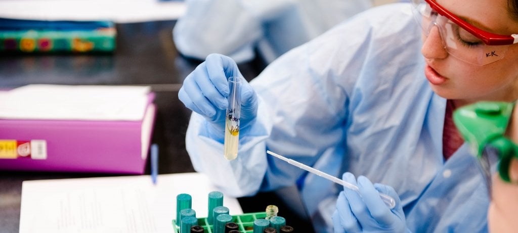 woman in lab safety gear wearing goggles and holding a test tube