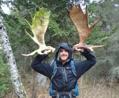 A student researcher at Isle Royale holds up moose antlers with the forest in the background.