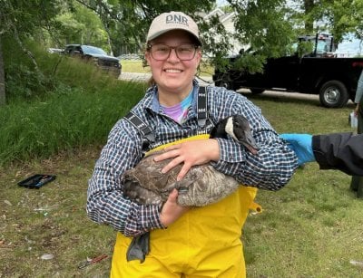 Blissick stands outside, grinning and holding an adult Canadian goose.