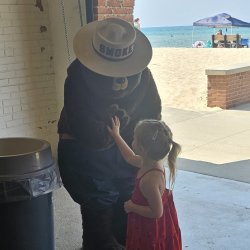 Smokey the Bear high-fives a young child inside an awning. Behind them, the sun shines on a sandy beach.