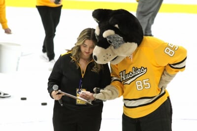 Ruby holding a microphone confers with Blizzard over a clipboard on ice.