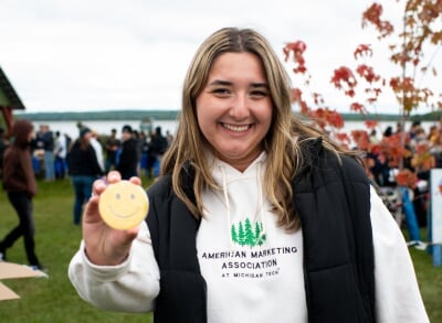 Ruby Walker, wearing an American Marketing Association at Michigan Tech sweatshirt, holds a smiley face button at K-Day.