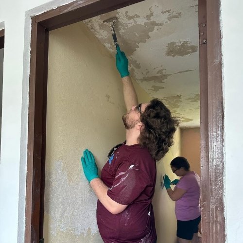 man paints door frame of a house