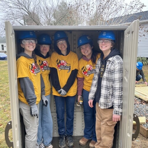 group of students wearing safety gear pose inside a wooden box