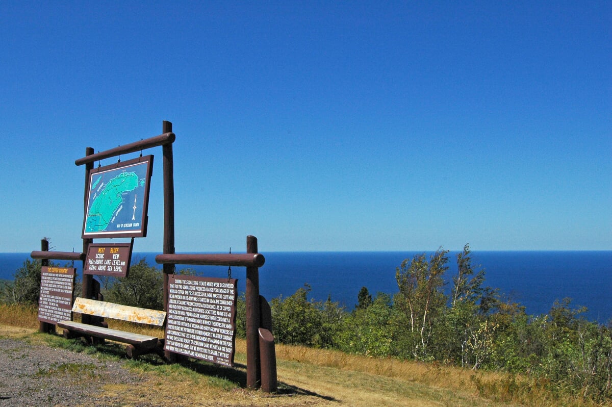 Brockway Mountain Signs about Copper Harbor overlooking trees and water.