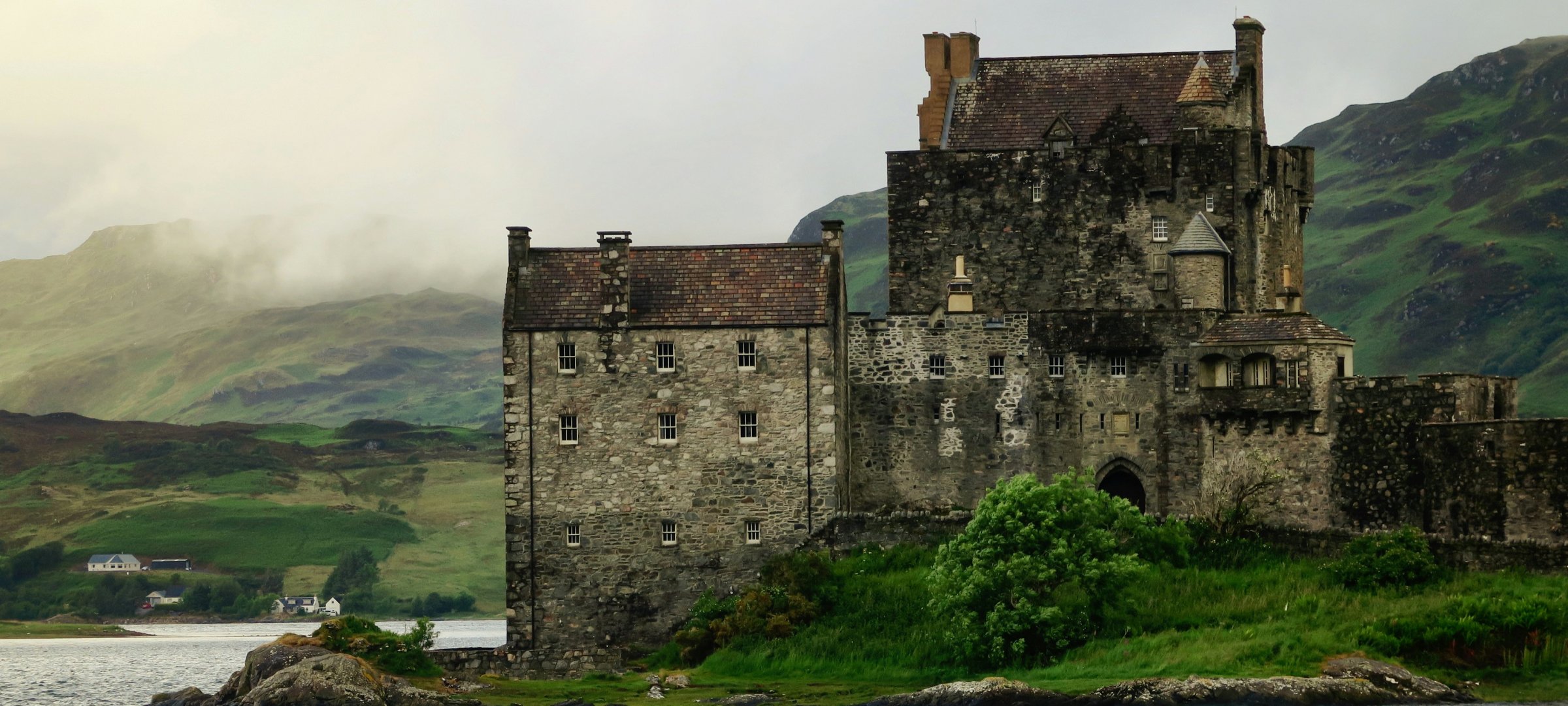 A castle by the lake with hills in the background in Scotland