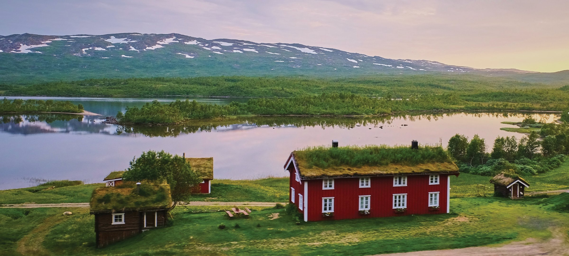 A cabin by the lake with hills in the background in Sweden