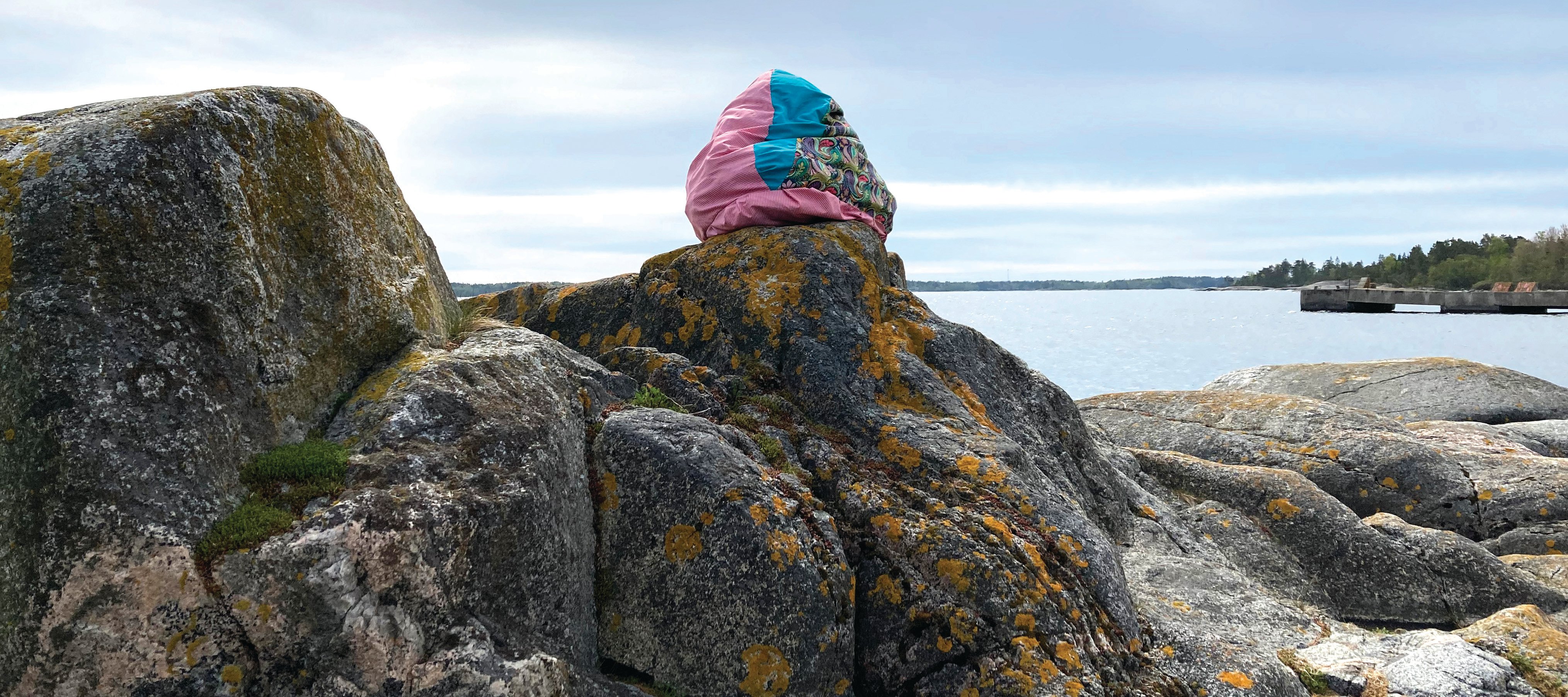 A soft, bright sculpture sitting on a rock in front of water
